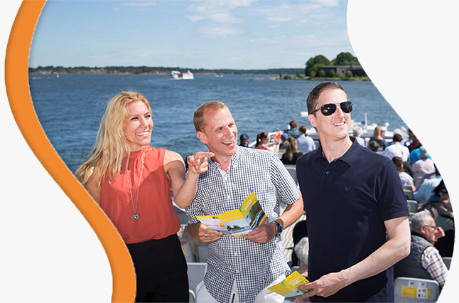 Three happy tourists on a sightseeing boat tour, holding Helsinki Card brochures, enjoying the scenic waterfront views included with the Helsinki Card.